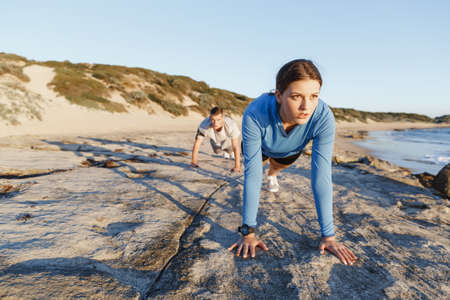 Young couple of man and woman doing push ups on ocean beach