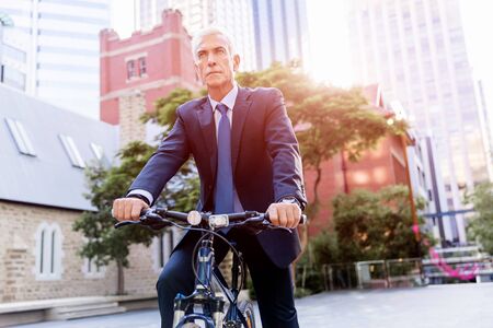 Successful businessman in suit riding bicycleの写真素材