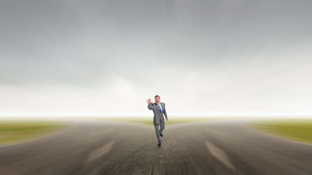 Young businessman in suit running on asphalt roadの写真素材