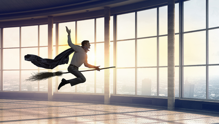 Young businessman flying on broom in modern interiorの写真素材