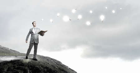 Young handsome businessman with old book in hands on rock topの写真素材