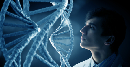 Young thoughtful male doctor looking at DNA molecule imageの写真素材