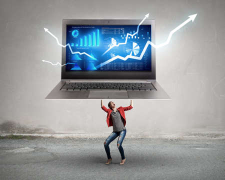 Elegant businesswoman lifting huge laptop above her headの写真素材