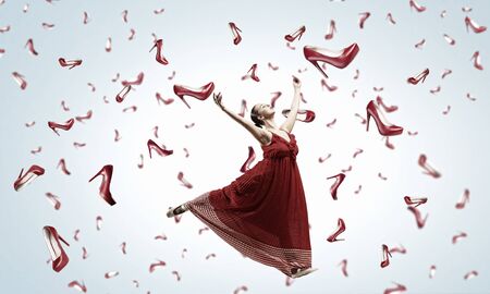 Beautiful young woman in dress under rain of falling shoesの写真素材