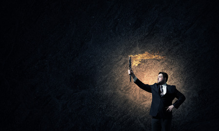 Young businessman in darkness holding burning torch in handの写真素材