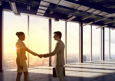 Businessman and businesswoman in elegant interior shaking hands against panoramic windowの写真素材