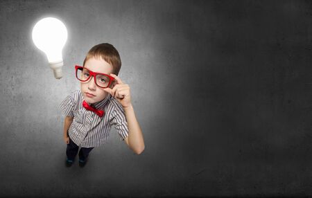Top view of cute schoolboy in red glasses on chalkboard background