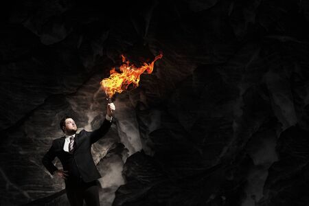Young businessman in darkness holding burning torch in handの写真素材