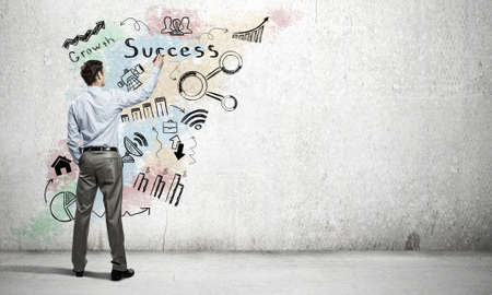 Businessman standing with back and drawing ideas on wallの写真素材