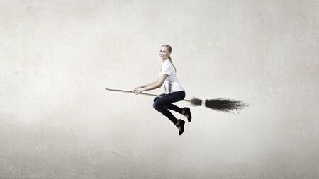 Young girl in casual flying on broom high in skyの写真素材