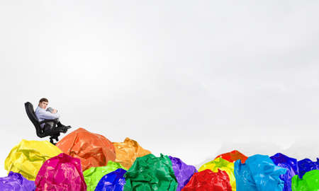 Businessman in chair and many crumpled balls of colorful paper as creativity signの写真素材