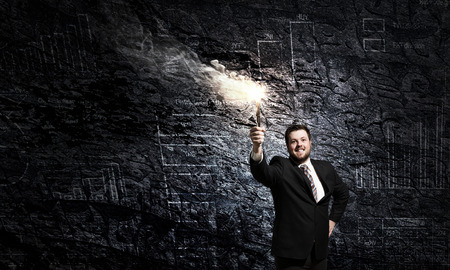 Young businessman in darkness holding burning torch in handの写真素材