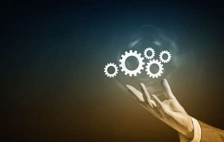 Businessperson hand holding gears and cogwheels in palmの写真素材