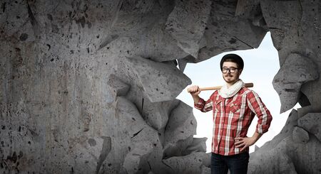 Young man with baseball bat in anger breaking wallの写真素材