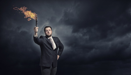 Young businessman in darkness holding burning torch in handの写真素材