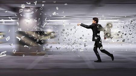 Young businessman walking with wind up key in his backの写真素材
