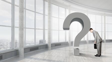 Young businessman in interior leaning on big question markの写真素材