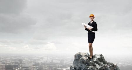 Attractive woman engineer wearing helmet with paper project in handsの写真素材