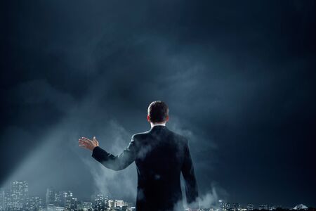 Back view of businessman with suitcase standing in spotlightの写真素材