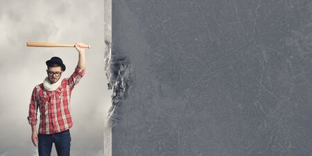 Young man with baseball bat in anger breaking wallの写真素材