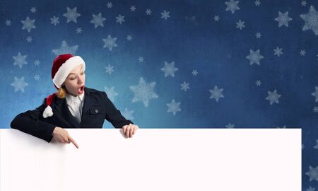 Woman in Santa hat pointing with finger at blank banner. Place for your textの写真素材
