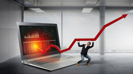 Young businessman on huge laptop making red arrow graph growの写真素材