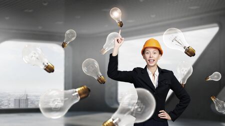 Attractive woman engineer in helmet with finger up and glass light bulbs in airの写真素材