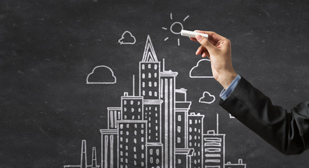 Close up of hand drawing urban city building on chalk boardの写真素材