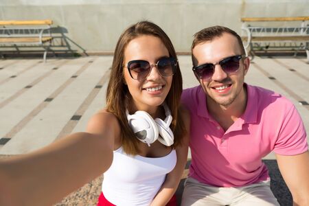 Happy young loving couple making selfie and smiling while sitting together in parkの写真素材
