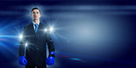 Determined businessman in suit and boxing gloves in lights of stageの写真素材