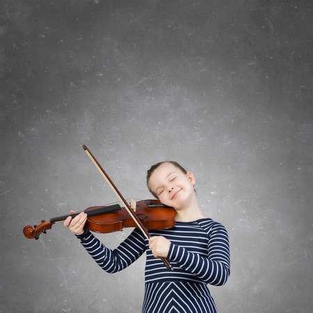 Cute girl of school age playing violin with pleasureの写真素材