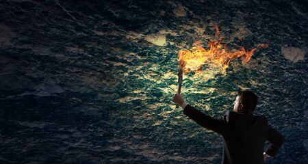 Young businessman in darkness holding burning torch in handの写真素材