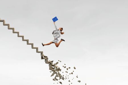 Young woman walking up collapsing staircase representing success conceptの写真素材