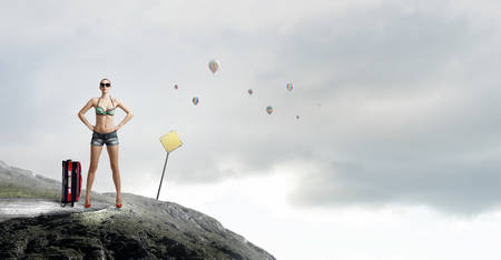 Beautiful woman in swimsuit standing on rock topの写真素材