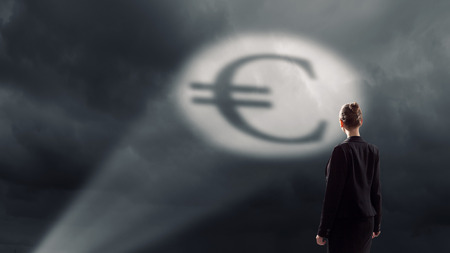 Businesswoman standing with back in darkness and euro sign in spotlightの写真素材