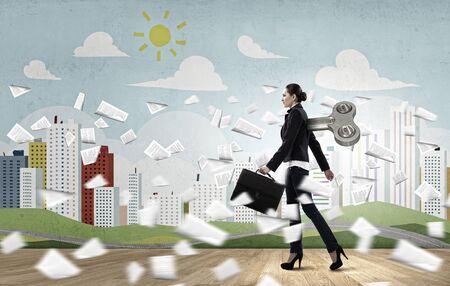 Young businesswoman walking with wind up key in her backの写真素材