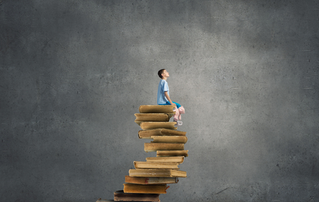 Cute little boy with toy bear sitting on pile of booksの写真素材
