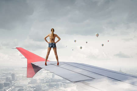 Beautiful woman in swimsuit standing on airplane wingの写真素材