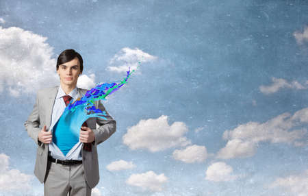 Young businessman acting like super hero and tearing his shirt offの写真素材