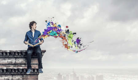 Guy sitting on building roof and reading bookの写真素材