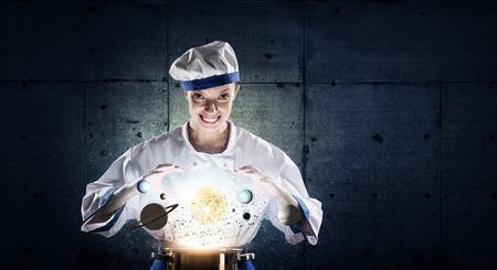 Pretty woman cook in hat and apron with doing magic above potの写真素材