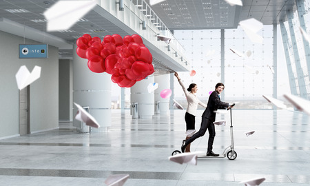 Young cheerful businesspeople riding scooter in officeの写真素材