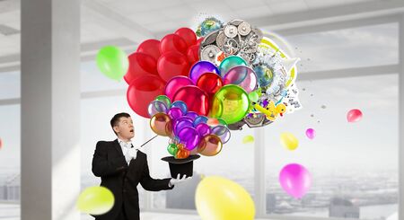 Young cheerful businessman making tricks with magic hatの写真素材