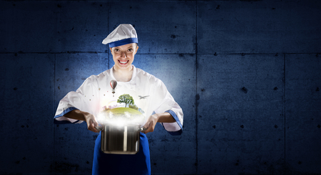 Pretty woman cook in hat and apron with pot in handsの写真素材