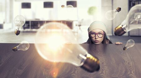Attractive student girl in red glasses peeping from under tableの写真素材