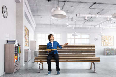 Guy sitting on wooden bench and reading bookの写真素材