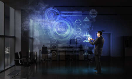 Adult businessman in office dark interior using tablet pcの写真素材