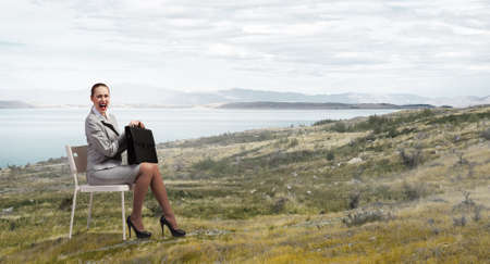 Young pretty businesswoman sitting on chair with briefcase in handsの写真素材