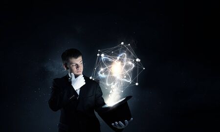 Young cheerful businessman making tricks with magic hat
