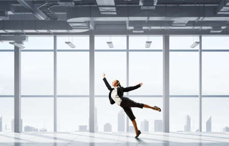 Young dancing businesswoman in suit in modern interiorの写真素材